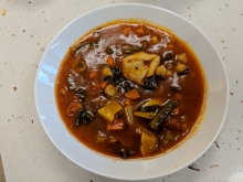 A white bowl filled with a tomato based soup with vegetables and pasta